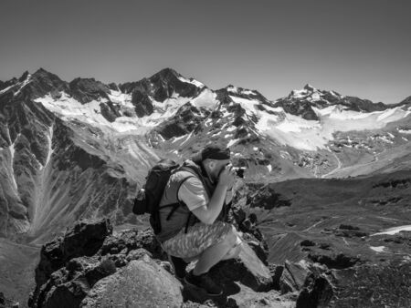 A man with a camera sitting on a rock high in the mountains is taking pictures. Black and white...