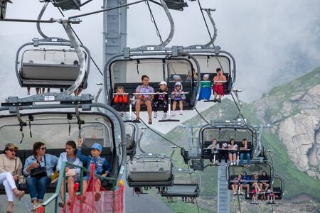 Krasnaya Polyana. Russia. July 28, 2019: Tourists climbing to the mountain peaks through the clouds in the open cabins of the cable car. Mountain tourist resort of Russia in the vicinity of the city of Sochi.のeditorial素材