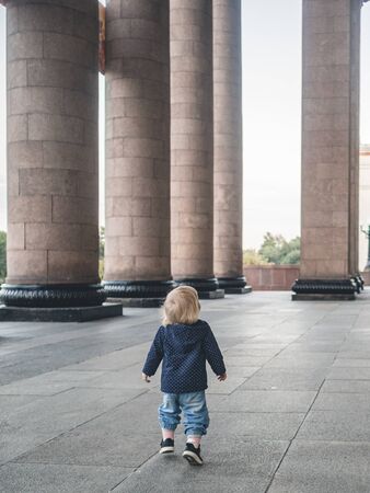 A little girl runs under the arch of a monumental building past a granite colonnadeの写真素材