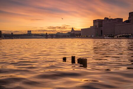 Sunset on the river in the city of Moscow. Fragments of pipes stick out of the water. A seagull flies against a background of orange sunset sky.の写真素材