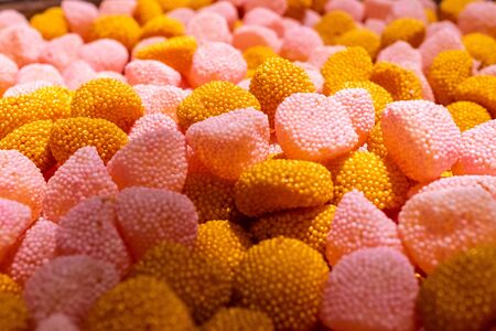 Bright yellow, gold and pink marmalade chewing sweets in the shape of berries. Sweet beautiful delicacy made from gel fruit juices. Colorful background. Randomly heaped goodies.の写真素材