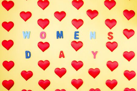 Multi-colored inscription Women's Day in the middle of rhythmically arranged silk red hearts on a...