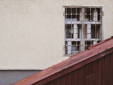 A yellow wall on which an old dirty window with a metal grill is obliquely closed with corrugated...