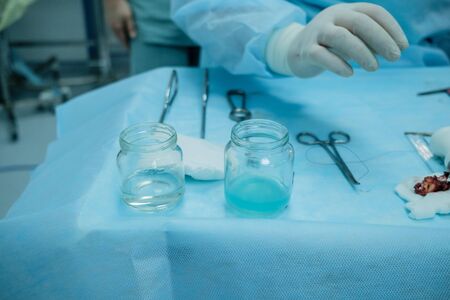 Sterile surgical instruments and glass containers with solutions on the table during a surgical operation. Above the table are the hands of a surgeon in latex gloves.の写真素材