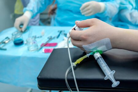 Hand of the patient lying on the operating table. On the finger is a pulse oximeter sensor. In the hand, a catheter with a syringe containing anesthesia. The patient is sleeping.の写真素材