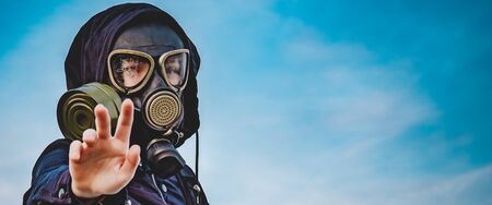 Banner. Girl in a black gas mask and dark clothes with a hood against the sky. The girl holds out her hand as a warning and a request for help. A global catastrophe of coronavirus infection.の写真素材