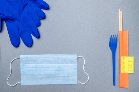 A fork, chopsticks, a medical mask and blue latex gloves and a sticker with the inscription covid-19...
