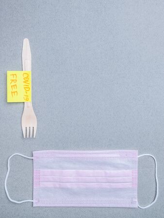 Wooden fork, pink medical mask and sticker with the inscription covid-19 free on a gray background. The concept of delivering safe, uninfected food during the quarantine coronavirus. Layout copy spaceの写真素材