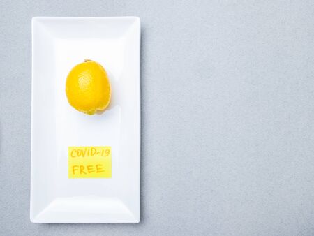 Lemon lies on a blue medical mask inside a white rectangular ceramic plate on a gray background....