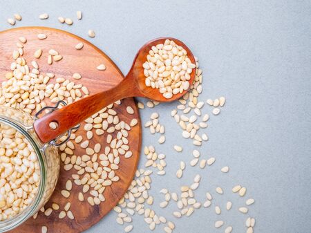 Layout. Glass jar with nuts of Siberian cedar standing on a wooden stand on a gray background. Nearby lies a wooden spoon. Nuts scattered on the surface. Food rich in vitamins and minerals. Copy spaceの写真素材