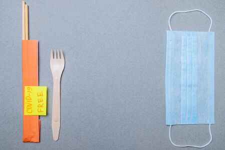 Fork, chopsticks, medical mask and sticker with the inscription covid-19 free on a gray background. The concept of delivering safe, uninfected food during the quarantine coronavirus. Layout Copy spaceの写真素材
