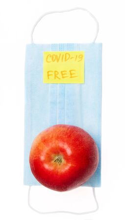 Flat lay. Red apple on a blue medical mask. Isolated. Yellow sticker with the inscription COVID-19 FREE. The concept of safe food.の写真素材