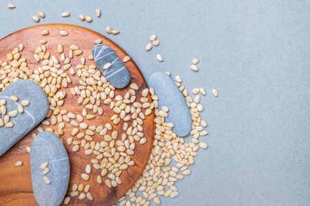 Flat lay. Oval gray stones on a wooden stand on a gray background in a placer of Siberian cedar nuts. Organic plant foods rich in vitamins, trace elements and energy. Copy spaceの写真素材