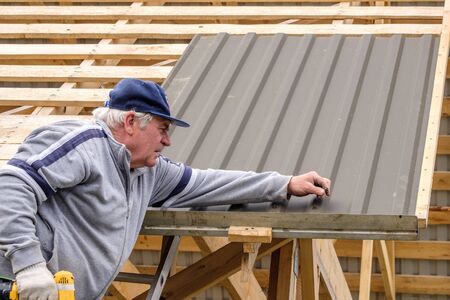 Senior builder man with a screwdriver screwing a roofing sheet to the roof.の写真素材
