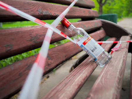 Moscow, Russia. May 14, 2020. The bench in the city park is wrapped in a red and white signal tape. On the bench is an empty bottle of vodka. Limitations during quarantine of coronavirus.のeditorial素材