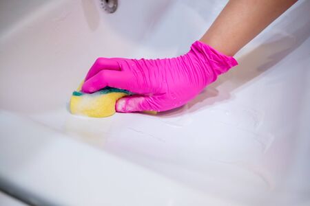 A hand in a pink glove washes a washbasin in the bathroom with a sponge with foaming detergent. Cleaning company cleans the house. Disinfection of the senile node from viruses and bacteria.の写真素材