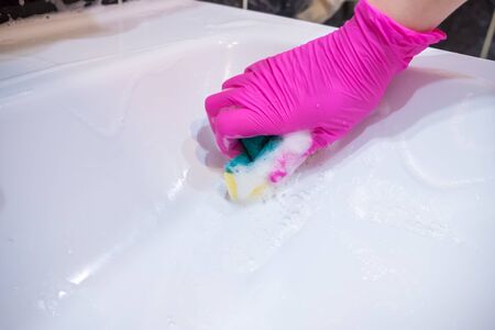 A hand in a pink glove washes a washbasin in the bathroom with a sponge with foaming detergent. Cleaning company cleans the house. Disinfection of the senile node from viruses and bacteria.の写真素材