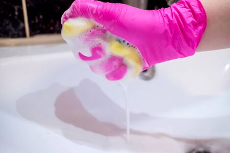 A hand in a pink glove washes a washbasin in the bathroom with a sponge with foaming detergent. Cleaning company cleans the house. Disinfection of the senile node from viruses and bacteria.の写真素材