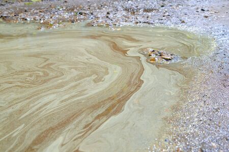 Dirty puddle on a broken road with yellow stains from pollen of plants. Pattern from pollen...