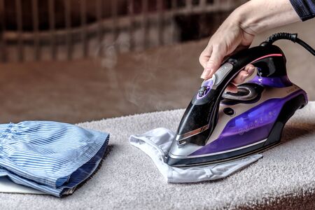 Closeup female hand ironing clothes on the table. Puffs of hot steam.の写真素材