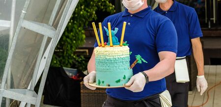 The waiters are holding a birthday cake with candles. Children's birthday party. The waiters have...