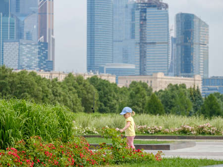 Blond-haired girl baby admires the flowers against the backdrop of skyscrapers.の写真素材