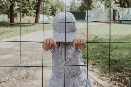 Little baby girl behind bars. The child holds onto the bars of the lattice.の写真素材