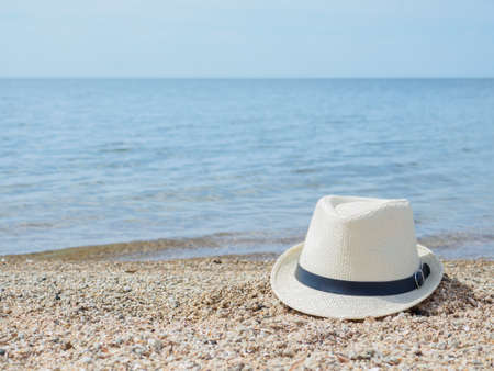 A white straw hat lies on the sand by the water. Sea beach on a summer sunny day. Sea vacation...