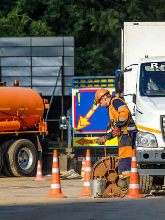 Moscow. Russia. 06 September. 2020 Workers in orange uniforms and protective helmets serve the sewer through an open manhole cover on the street. The work of public utilities in the cityのeditorial素材