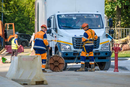 Moscow. Russia. 06 September. 2020 Workers in orange uniforms and protective helmets serve the sewer through an open manhole cover on the street. The work of public utilities in the cityのeditorial素材