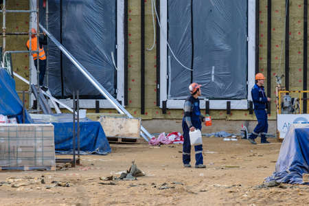 Moscow. Russia. 06 September 2020 Construction workers in uniforms and safety helmets at the construction site manually transfer construction materials. Summer day. Construction industryのeditorial素材