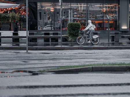 Moscow. Russia. 08 September 2020 View of a city street in the rain. A girl rides on a wet asphalt on a bicycle past glass windows that reflect the street. Autumn evening in the cityのeditorial素材