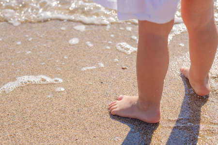 Baby feet close-up on the sand of the sea beach. Sea water washes the feet. Happy childhood. Rest at...