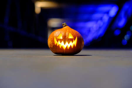 Halloween pumpkin in the dark on a blue industrial abstract background. Blurry colored lights. The decor of the night city in a festive Halloween theme. Copy space.の写真素材