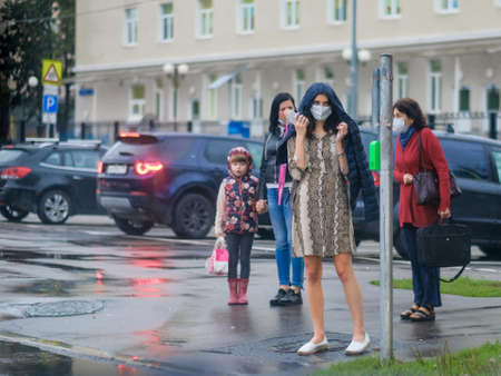 Moscow. Russia. September 08, 2020 A girl in a protective mask with a hood on her head and a smartphone in her hand stands on the sidewalk among people. Waiting for the second wave of coronavirus.のeditorial素材