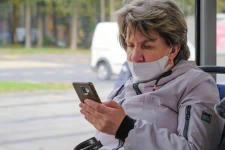 Moscow. Russia. September 29, 2020. A woman in a city bus reads the news on a smartphone screen. On the faces of passengers are protective masks. The second wave of the coronavirus pandemic.のeditorial素材