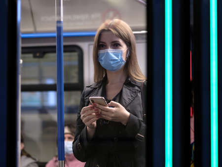 Moscow. Russia. September 25, 2020 A young woman in a subway car is holding a smartphone. On the faces of passengers are protective masks. Protection against viral infections in public transport.のeditorial素材