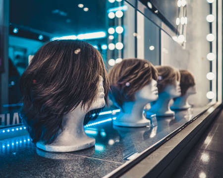 Female heads of mannequins in a row on a store window at night. Blue and white neon lights and glare on glass.の写真素材