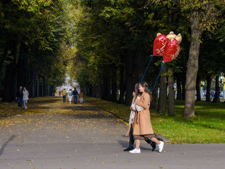 Moscow. Russia. October 11. Happy couple of girls in love with red balls on a date in a city park on an autumn sunny dayのeditorial素材