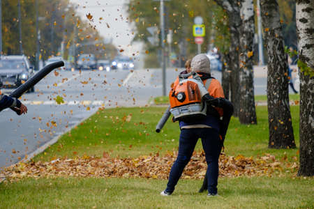 Moscow. Russia. October 11, 2020 Community workers use a blower to remove fallen leaves from city streets and parks.のeditorial素材