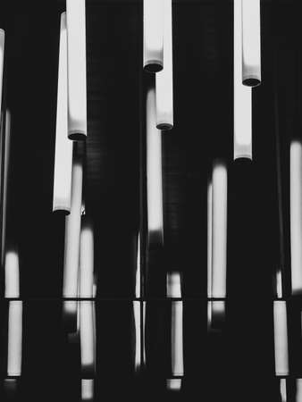 Several glowing cylindrical lamps in the dark. The cylinders are reflected in a glossy mirror surface. Abstract black and white image.の写真素材