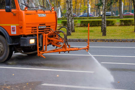 Moscow. Russia. October 11, 2020. An orange heavy truck washes autumn leaves off the asphalt street. The work of public utilities in the city. Autumn day.のeditorial素材