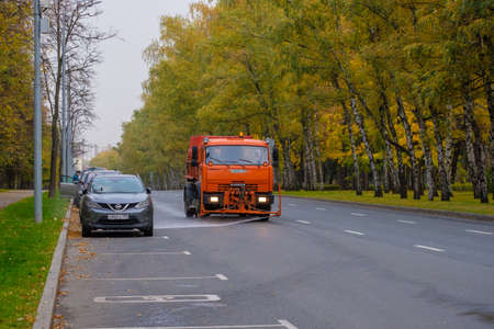 Moscow. Russia. October 11, 2020. An orange heavy truck washes autumn leaves off the asphalt street....
