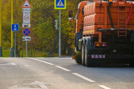 Rear view of an orange multifunctional heavy duty truck for cleaning an asphalt street. The car...