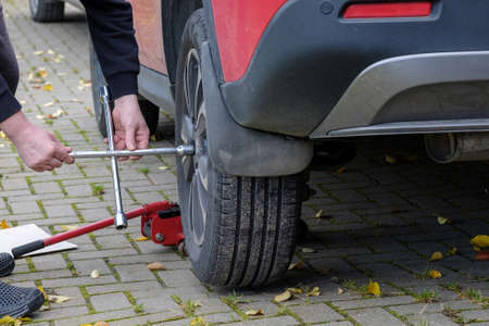 A wrench in the hands of an auto mechanic unscrews the bolts and nuts of a car wheel. Seasonal...