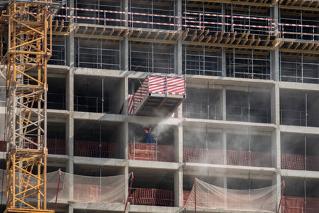 View of the facade of a multi-storey concrete monolithic building under construction. Fences and metal structures on the floors. Cement dust is flying in the air. High quality photoの写真素材
