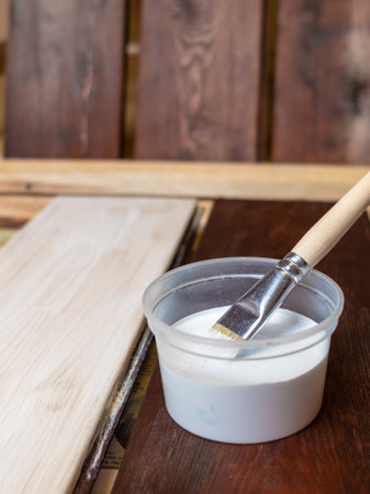 Selective focus. A container with paint and a brush. The horizontal boards are painted with white paint and a brush. Renovation and design. Place for your text. Copy space.の写真素材