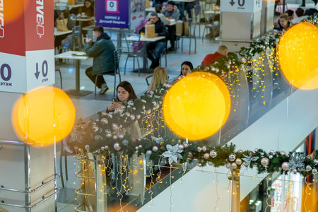 Moscow. Russia. December 8, 2020. People sit at tables in the Food Court mall on Christmas Eve. The interior is decorated with festive illumination to celebrate the new year.のeditorial素材