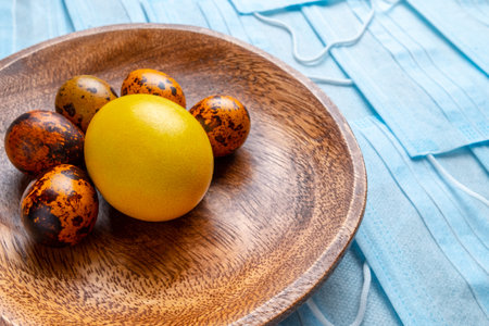 Colored easter eggs on a wooden plate on a background of blue medical masks. Flat lay. Easter holiday concept during quarantine epidemic. Copy space.の写真素材