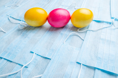 Colored Easter eggs on a background of blue medical face masks. Flat lay. Easter holiday concept during quarantine epidemic. Copy space.の写真素材